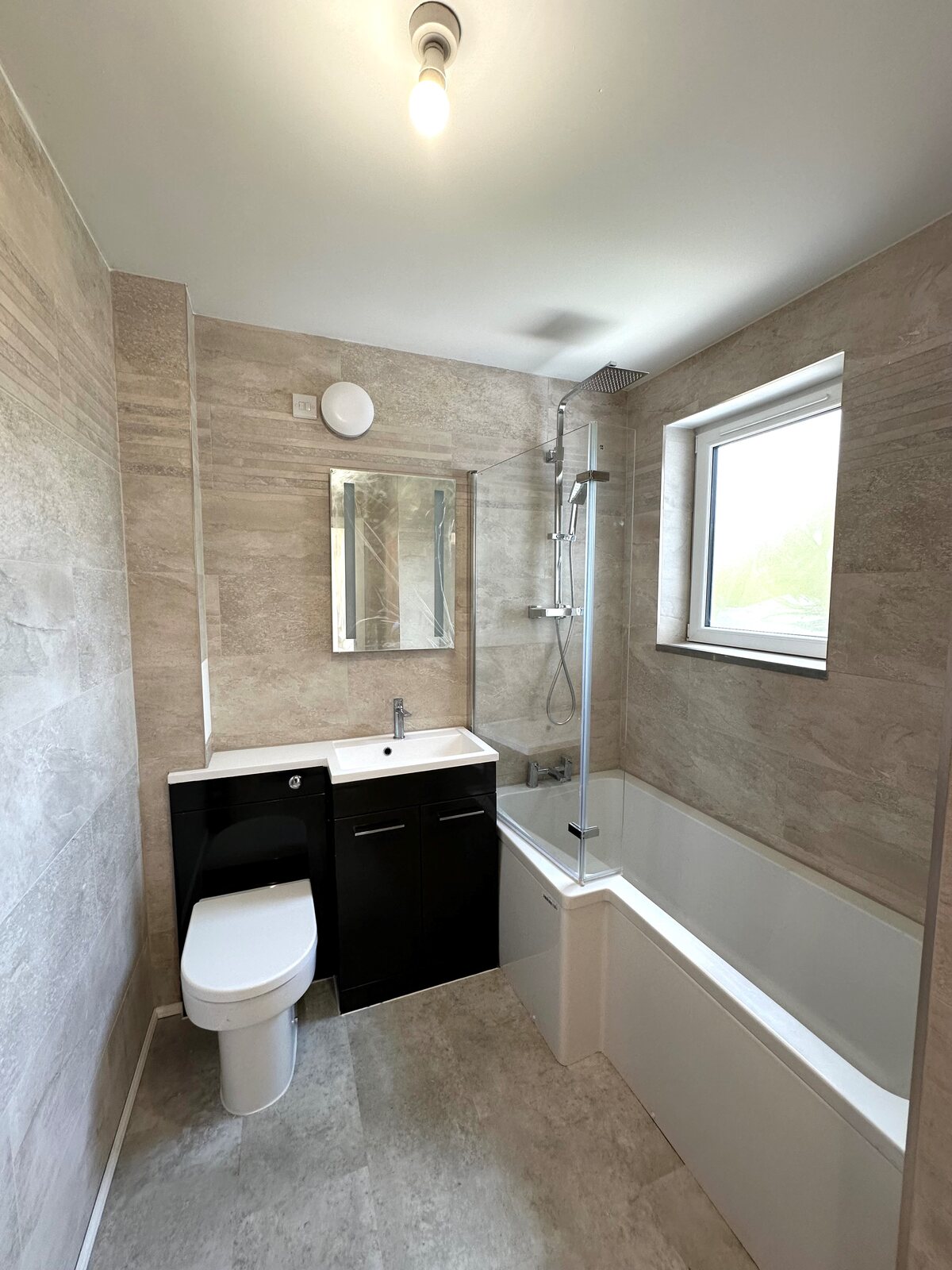 Completed bathroom with tiled walls, bath, rainfall shower and fitted vanity unit